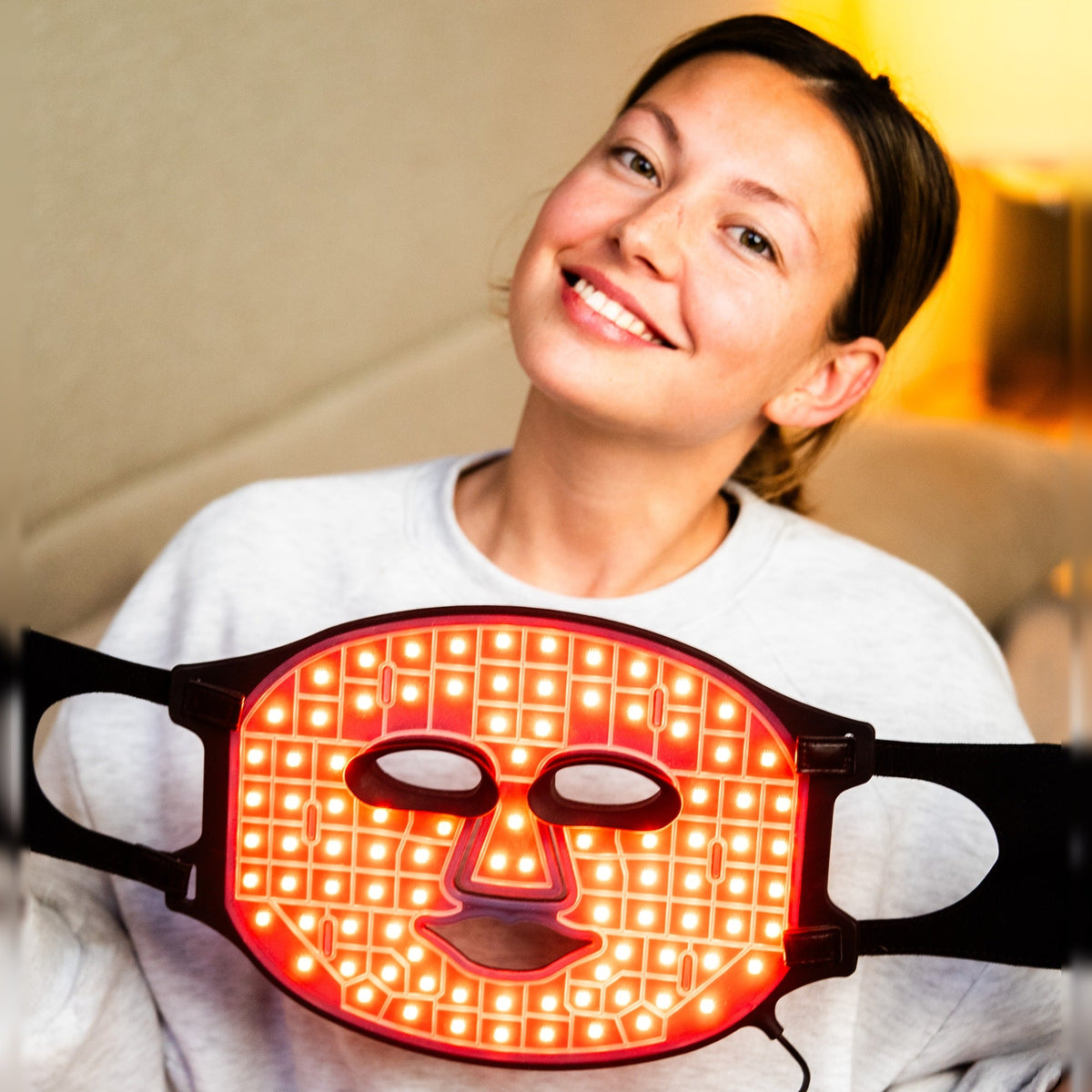 Kvinna som ler med Nordic Flow Betterskin LED-mask i rött ljus hemma