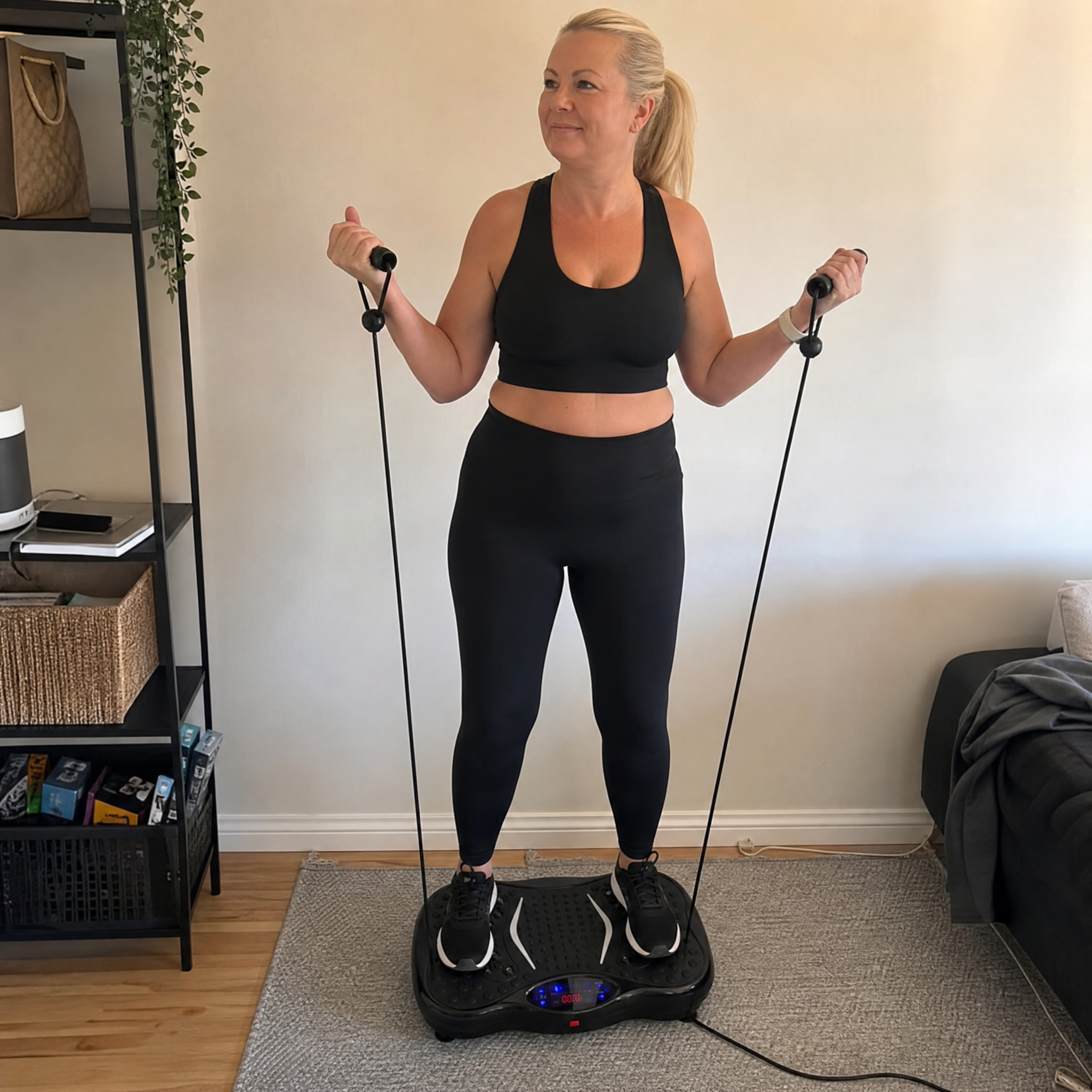 Kvinna tränar hemma på vibrationsplatta Vera FIT och drar i de medföljande träningsbanden för armar och överkropp i vardagsrummet